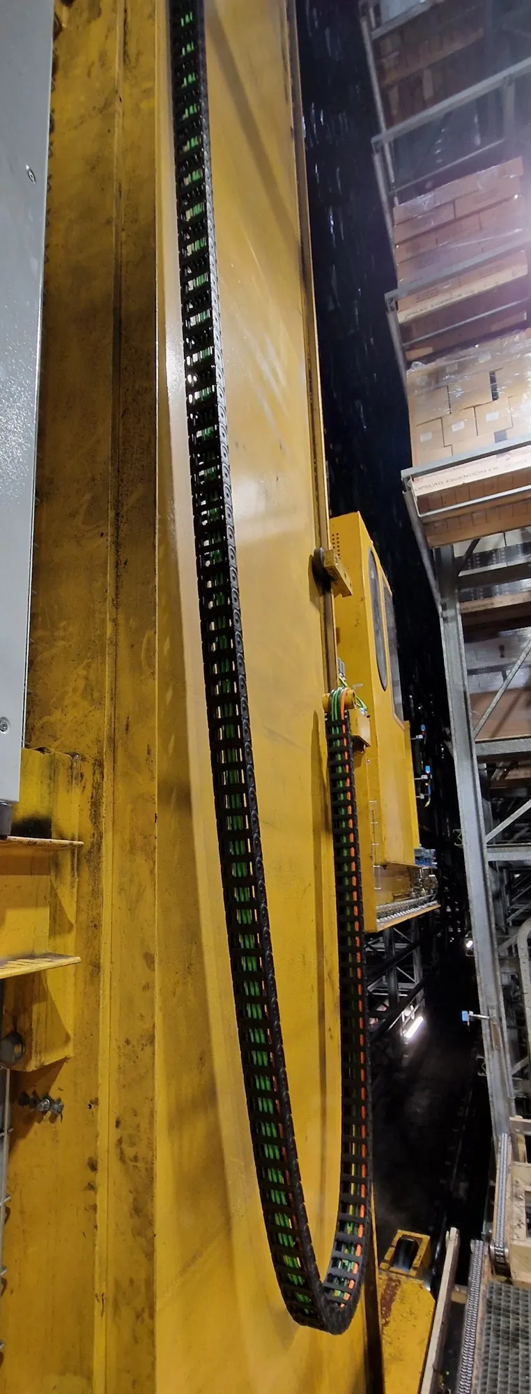 The cable carrier along the mast of the warehouse crane, next to the racks
