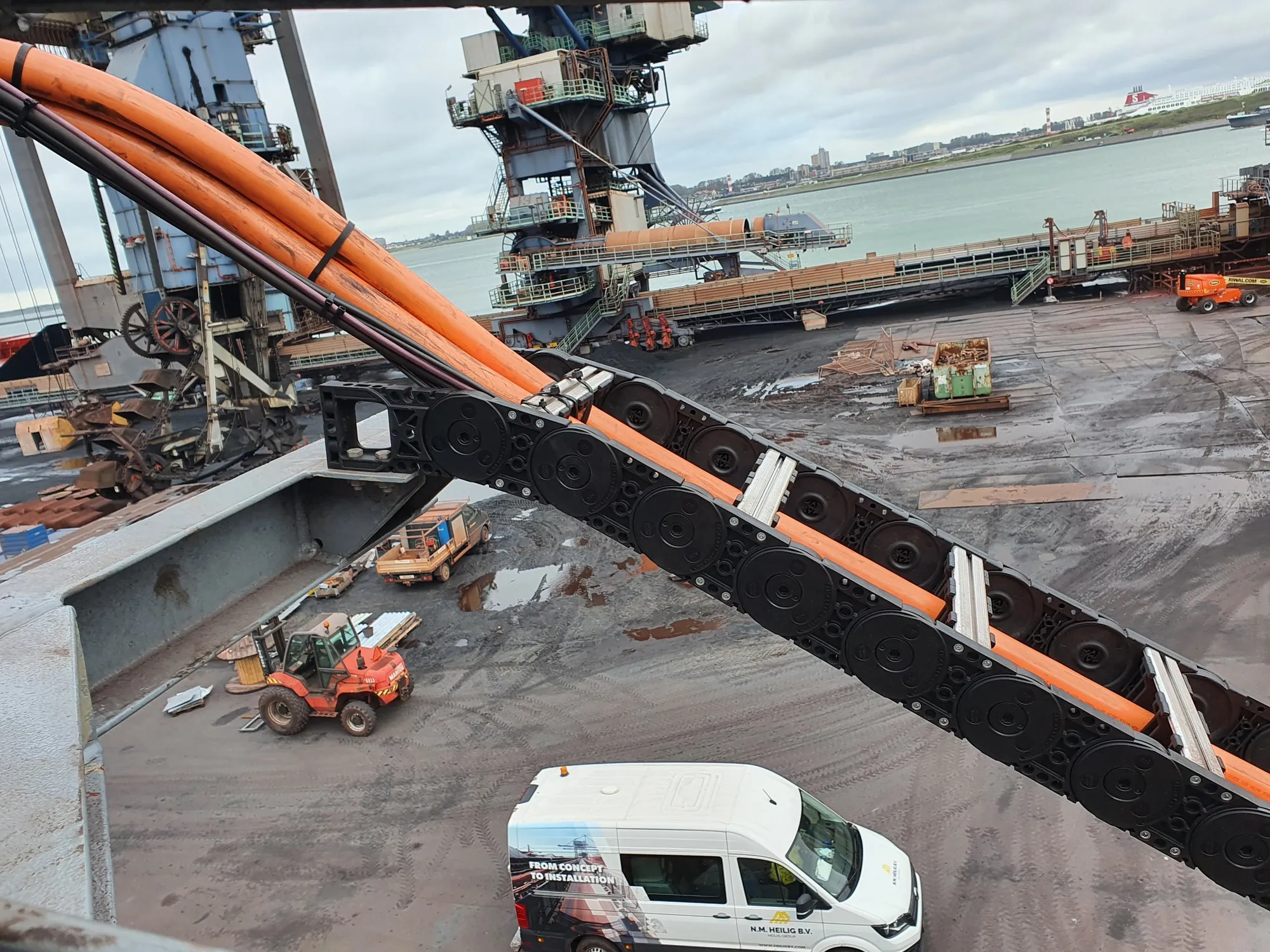 Cable carrier with orange cables on the extendable unloading arm, with the coal terminal in the background